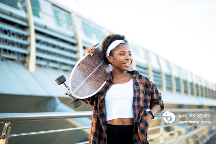 Portrait of happy african-american woman with skateboard. Young stylish woman with skateboard outdoors.