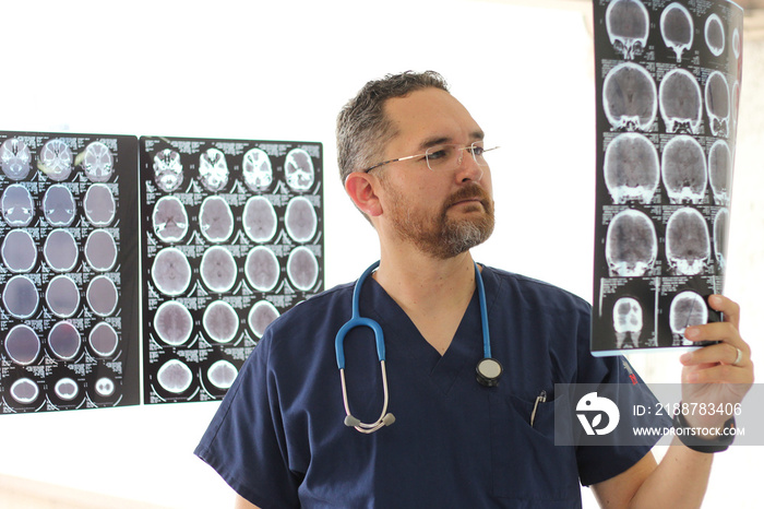 Young neurologist specialist medical doctor in glasses and beard analyzing brain scans on x-rays to find any disease in the patient