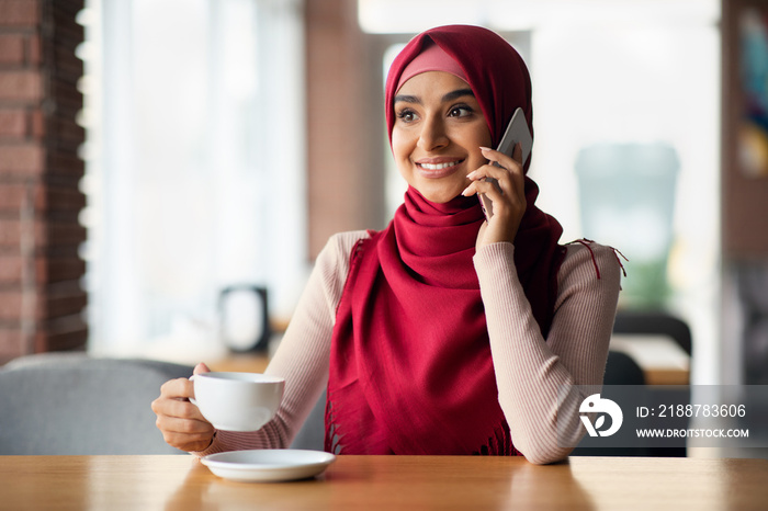 Happy middle eastern lady in hijab having phone conversation