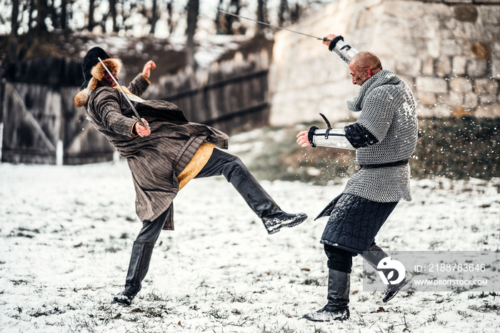 Battle of two warriors in armor with weapons fighting with swords in the snow