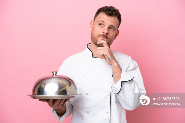 Young Brazilian chef with tray isolated on pink background having doubts and thinking