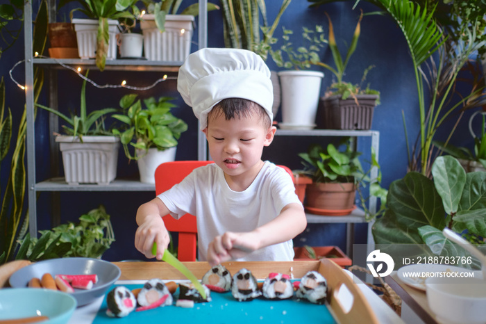 Cute happy smiling Asian little boy child wearing chef hat having fun preparing, cooking healthy Japanese food -  sushi roll at home, Fun activities for kindergarten kids concept