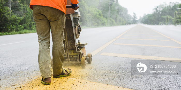 Worker using the thermoplastic spray marking machine to paint yellow line in road work construction.