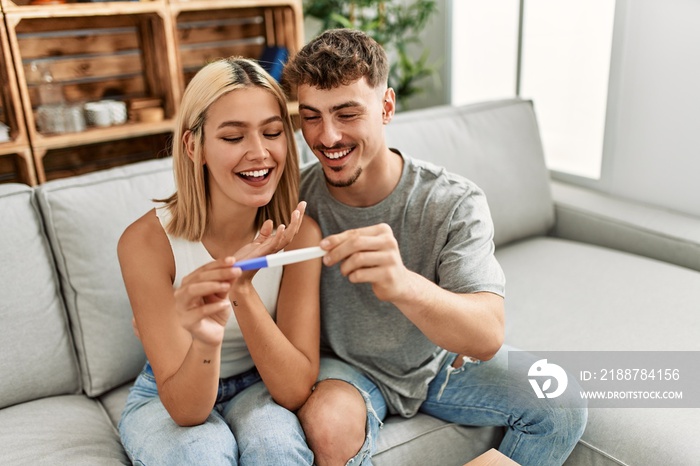 Young caucasian couple smiling happy holding pregnacy test at home.