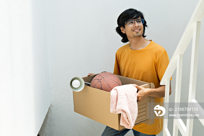 young man holding a moving box, climbing up stairs inside a building