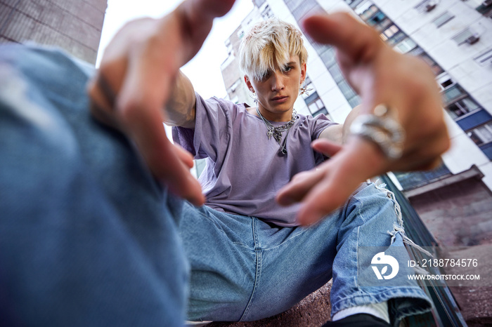 Close up of a teenage boy reaching a camera while crouching on the city street.