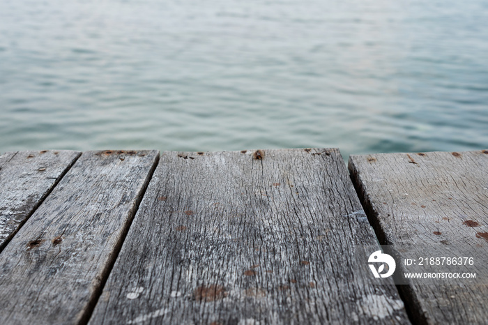 Wooden material table or counter bar with copy space and blurred background of ocean water. Selective focus at wooden surface in center.