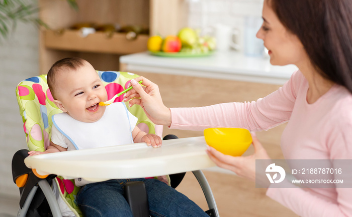 Young woman feeding her cute toddler in kitchen