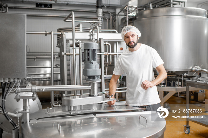 Portrait of a handsome worker in uniform near the stainless tank full with fermenting milk at the cheese manufacturing