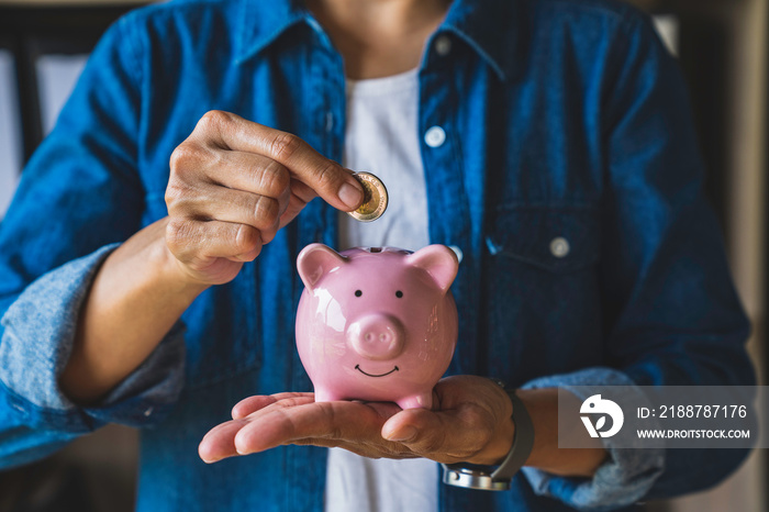 woman holds a coin in a pig-shaped piggy bank to save money for the future. after retirement and record keeping of income, expenditure, savings and financial concepts.