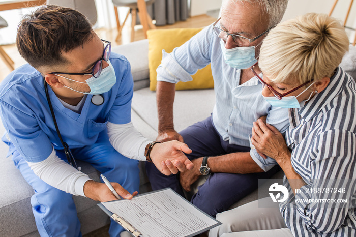 Male nurse talking to seniors patients with mask while being in a home visit.