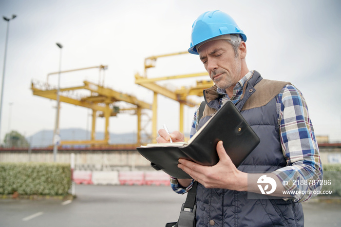 Mature construction worker inspecting work sight with notebook