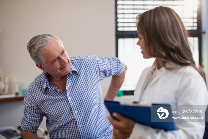 Senior male patient showing back ache to female doctor with file