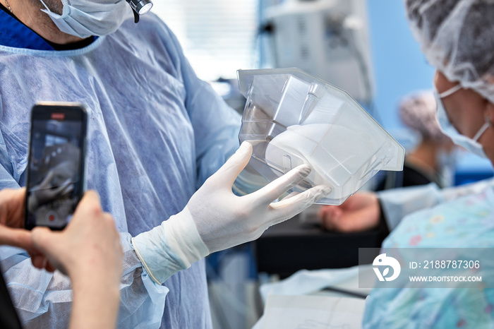 Surgeons during surgery with breast implants in their hands, installation of breast implants, surgery. Plastic surgery, breast correction, mammoplasty.