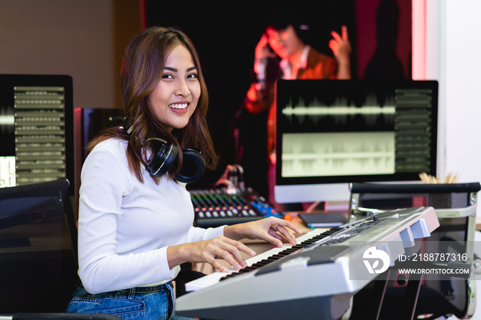 Asian producer woman in white shirt standing by sound mixing console. Happy female music composer artist with a man singer background