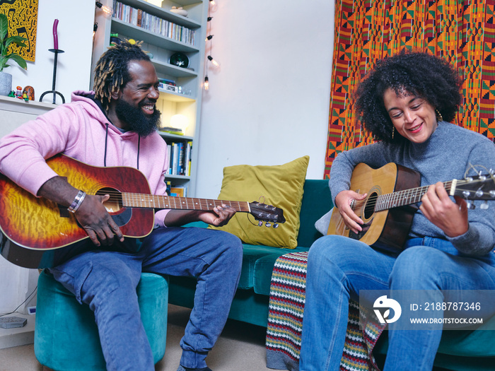 Couple playing acoustic guitars at home