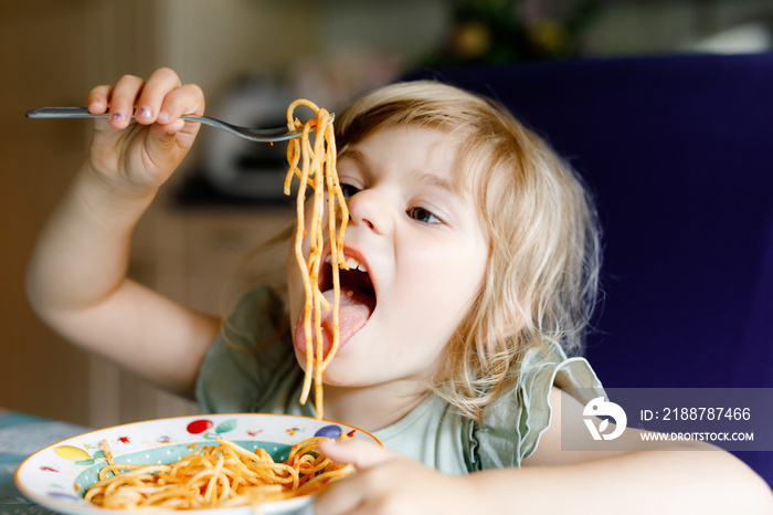 Adorable toddler girl eat pasta spaghetti with tomato bolognese with minced meat. Happy preschool child eating fresh cooked healthy meal with noodles and vegetables at home, indoors.