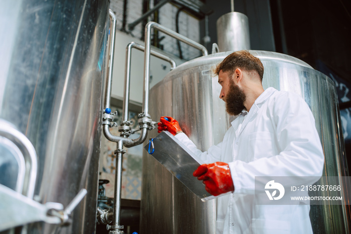 Caucasian male professional  technologist expert in white suit  operating production machine in food factory and doing quality control and holding checklist. Checking production in food industry.