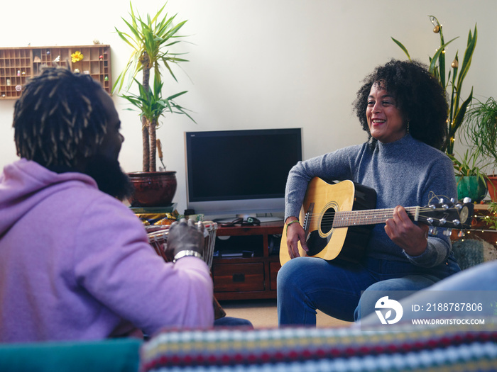 Couple playing acoustic guitars at home