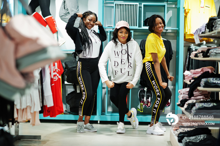 Three afican american women in tracksuits shopping at sportswear mall against shelves. Sport store theme.