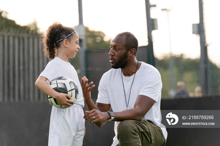 Man instructing girl (6-7) with ball on soccer field