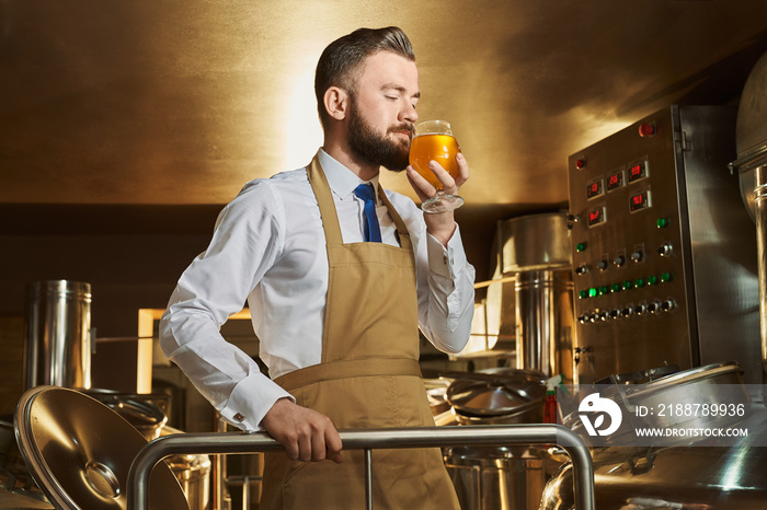 Male brewer smelling golden beer while working at factory