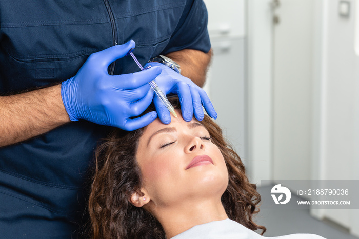 Close up of beautician expert’s hands injecting botox in female forehead.