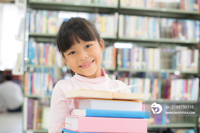 child girl holding a stack of books in the library