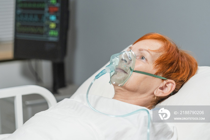 Elderly woman lying in hospital bed in oxygen mask on her face, she breathing hard during disease