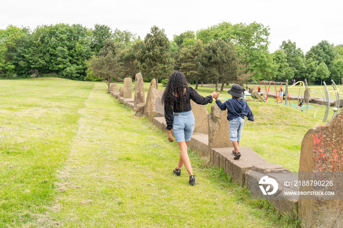 Mother helping son with walking on stone wall at playground