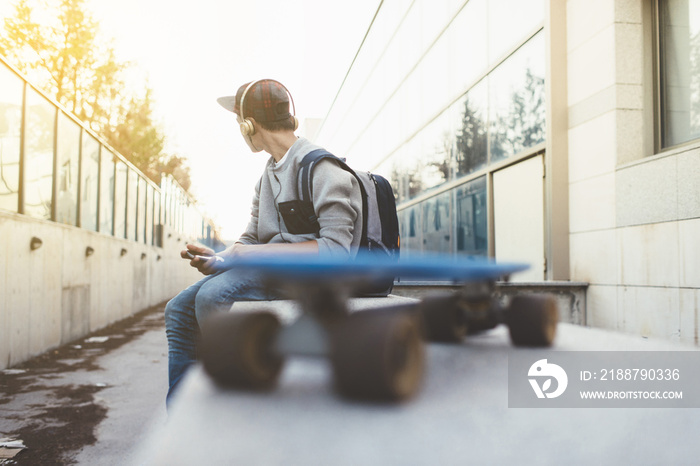 Young man looking at smartphone with skateboard and headphones