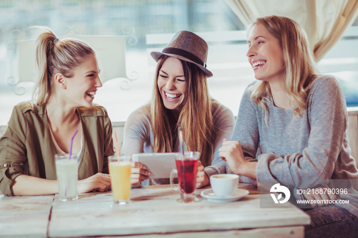 Female friends enjoying in conversation and drinking coffee in cafe and using digital tablet.