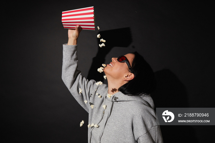 Young woman in 3D glasses eating popcorn while standing over black background