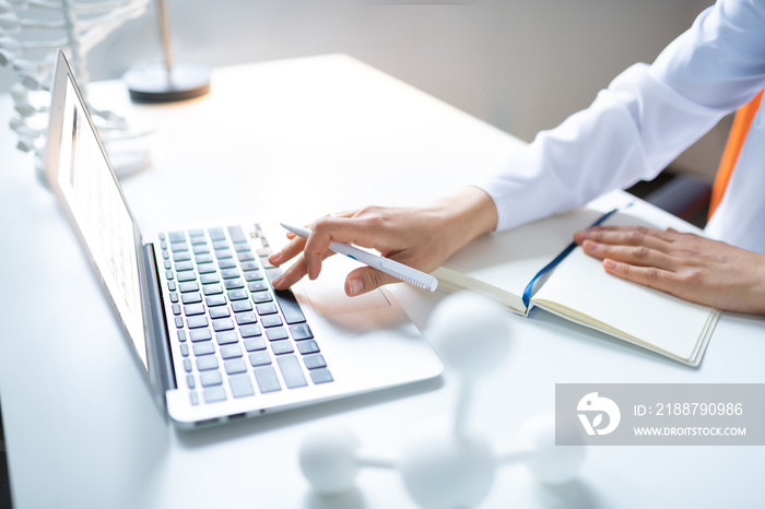 Scientist holding pen and typing something on laptop