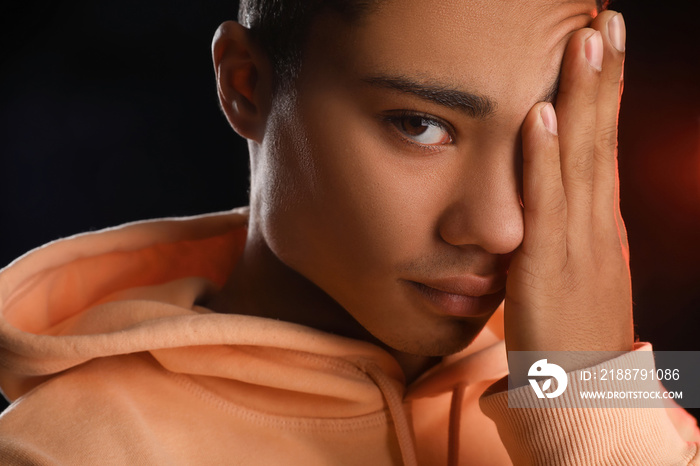 Tired African-American teenage boy in hoodie on black background, closeup