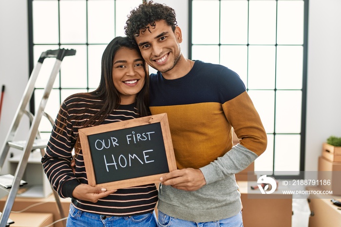 Young latin couple smiling happy holding our first home blackboard at new house.