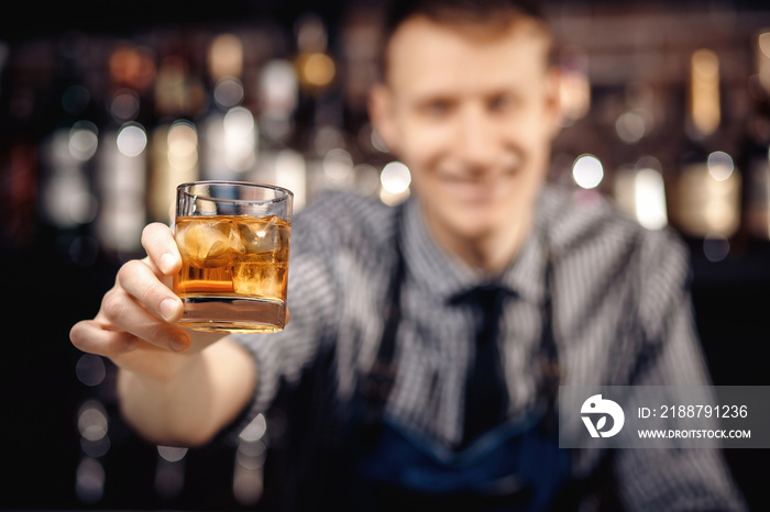 Barman holds out glass of whiskey with ice to male visitor. Concept rest in bar