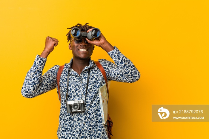 Young african tourist man standing against a yellow background holding a binoculars