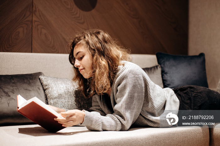 Teenager girl reading book on the couch at home