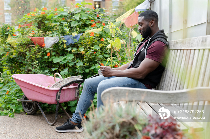 Man with smart phone sitting on bench in allotment