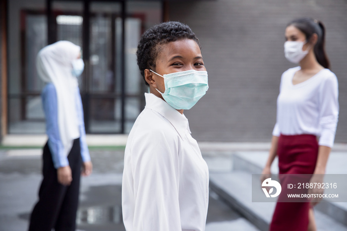 Happy smiling black African woman wearing face mask, observing new normal lifestyle of social distancing, keeping distance away from other people in public