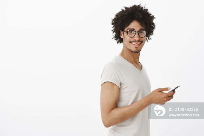 Guy using online map to find way during vacation in foreign city, standing in profile and turning at camera, smiling, holding smartphone, waiting for boyfriend in park, standing over gray background