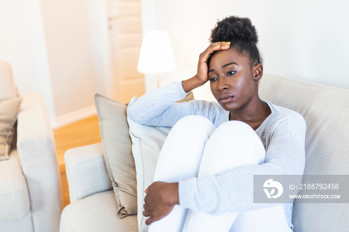 Sad thoughtful worried african american girl sit on sofa looking away feel depressed doubtful, lonely stressed upset young black girl thinking of psychological problem thinking regret about mistake