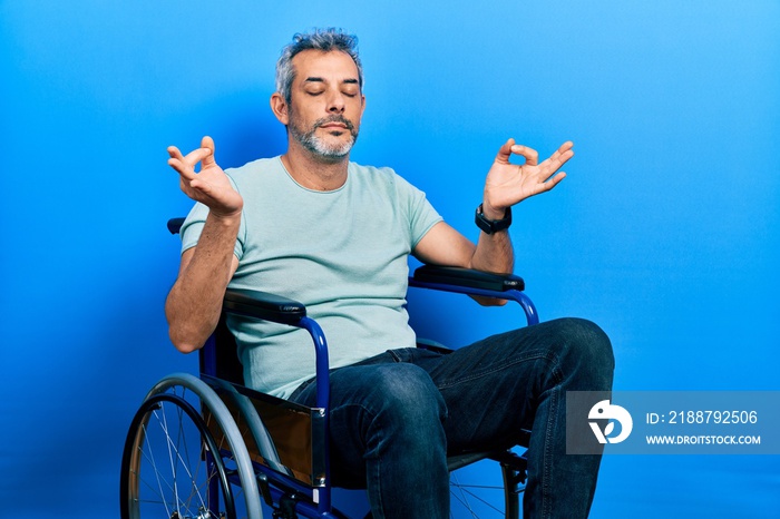 Handsome middle age man with grey hair sitting on wheelchair relaxed and smiling with eyes closed doing meditation gesture with fingers. yoga concept.