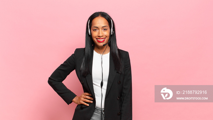 young black woman smiling happily with a hand on hip and confident, positive, proud and friendly attitude. telemarketing concept