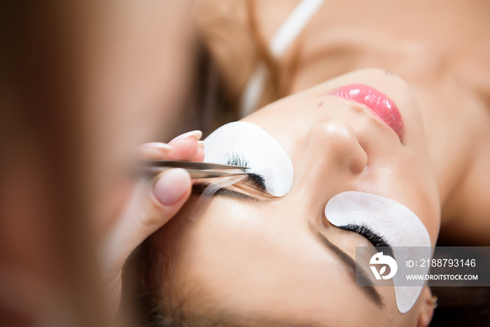 Beautiful young woman during eyelash extension in a salon.