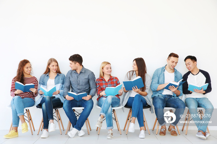 Group of people reading books while sitting near light wall