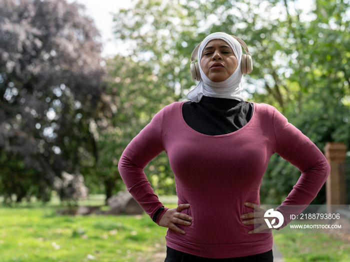 UK,Sutton,Woman in headscarf and headphones relaxing after workout in park