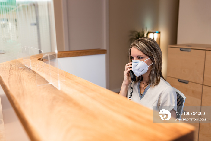 young woman answer the phone at the reception with coronavirus mask