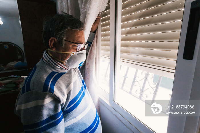 Selective focus of man with a mask confined in quarantine to prevent coronavirus spread to the window.